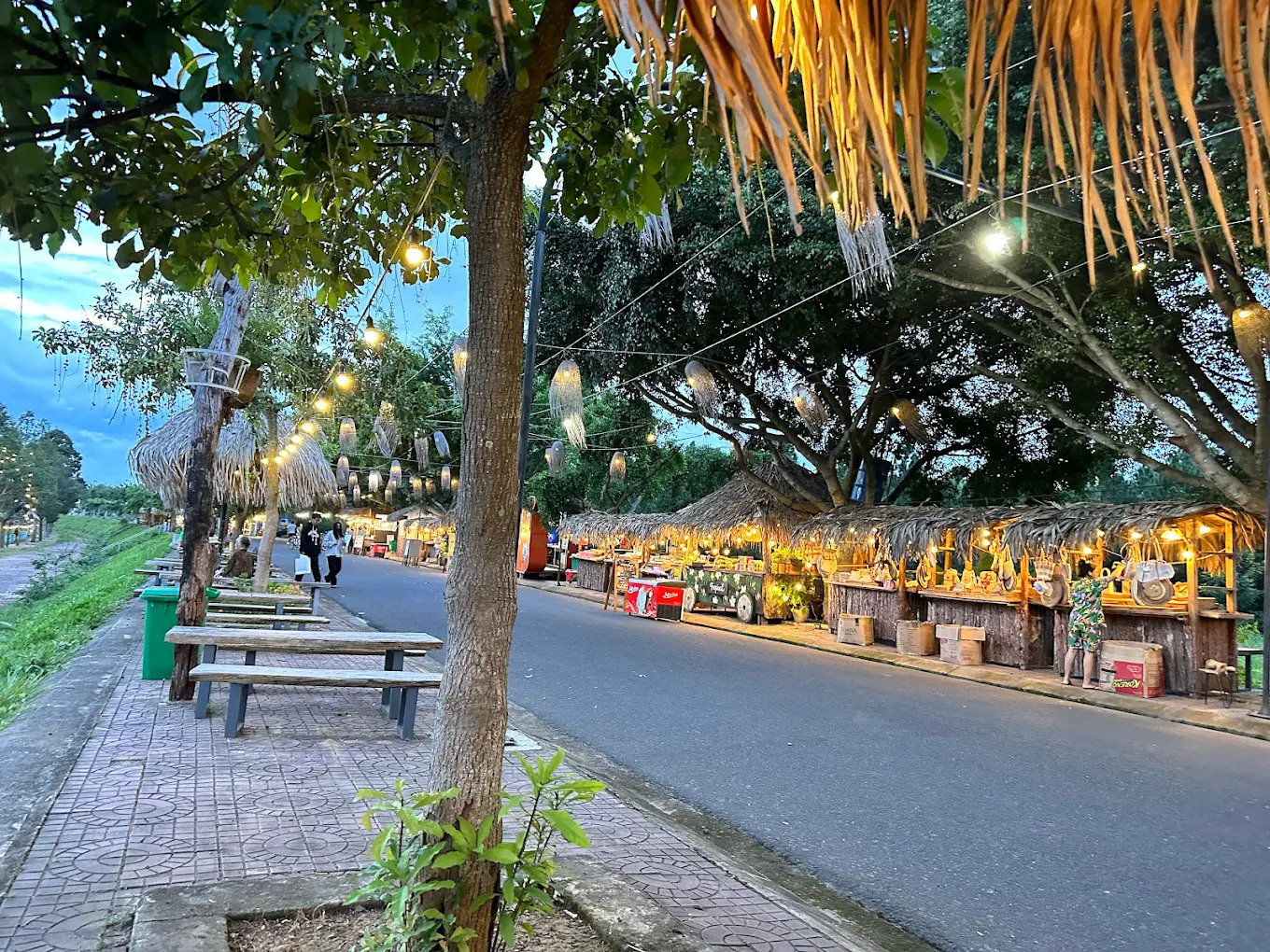 Dãy gian hàng lợp mái lá thủ công, sáng đèn rực rỡ bên đường