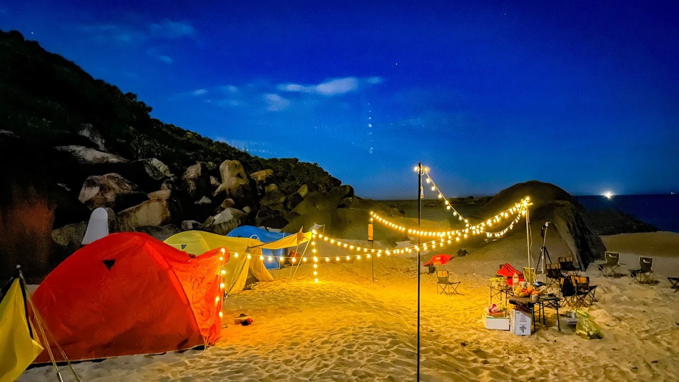 Không gian cắm trại ấm cúng, kết hợp giữa ánh đèn vàng nhẹ và khung cảnh núi đá bên biển tạo nên một buổi tối khó quên.